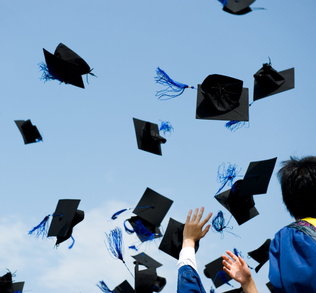 students celebrating graduation by throwing mortarboard caps into air